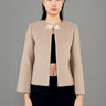 A woman stands in front view, wearing a stylish beige jacket with a round neckline and a decorative floral brooch at the front. The jacket has long sleeves and is paired with a black cropped top and dark trousers. 
一名女子站在正面，身穿時尚的米色圓領外套，胸前飾有花朵胸針。外套為長袖設計，內搭黑色露臍上衣和深色長褲。