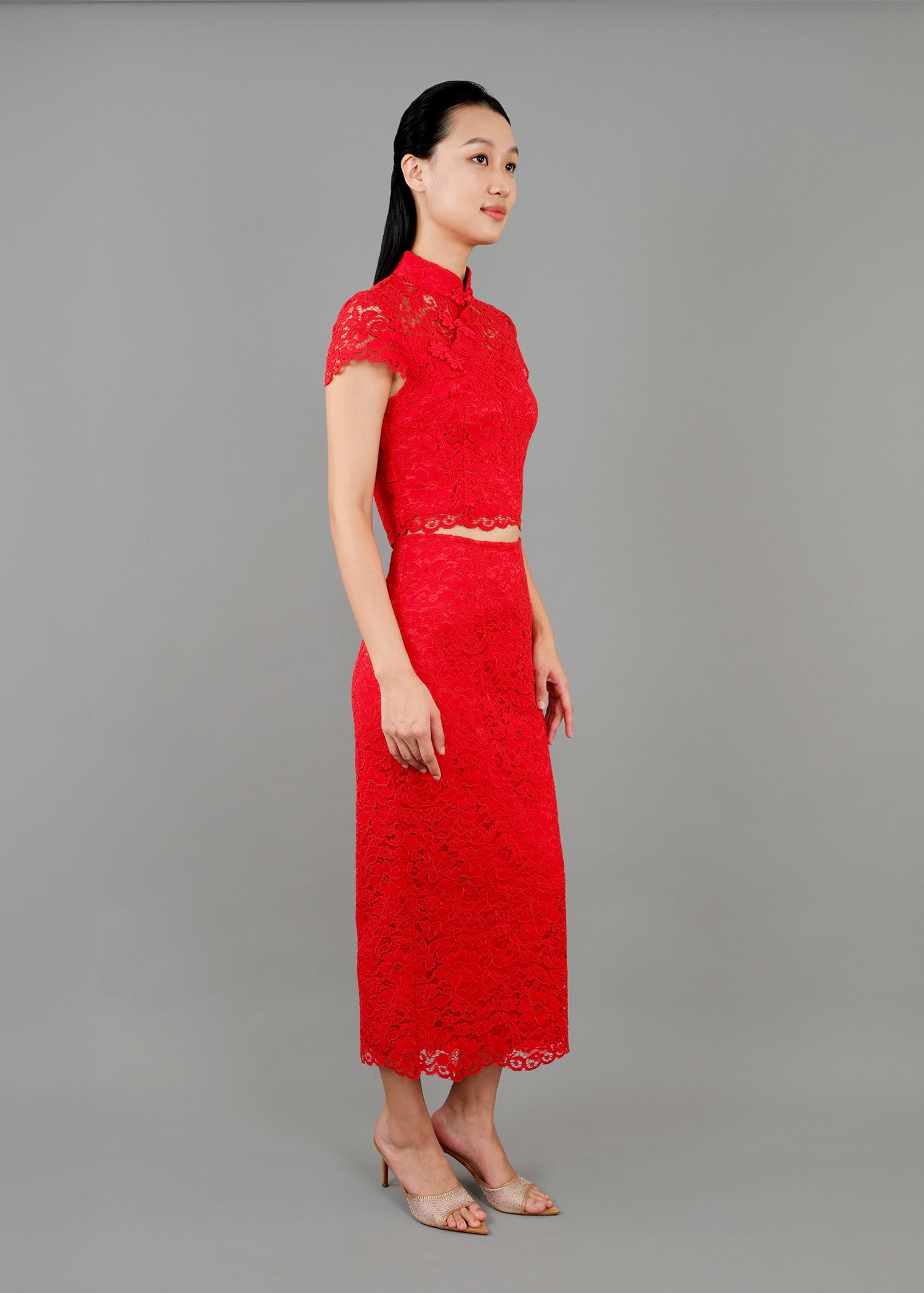 A woman stands in side view, wearing a red lace high-neck, short-sleeved dress that reaches mid-calf, featuring intricate lace detailing.
一名女子站在側面，身穿紅色蕾絲高領短袖連身裙，長及小腿中部，帶有精緻的蕾絲細節。