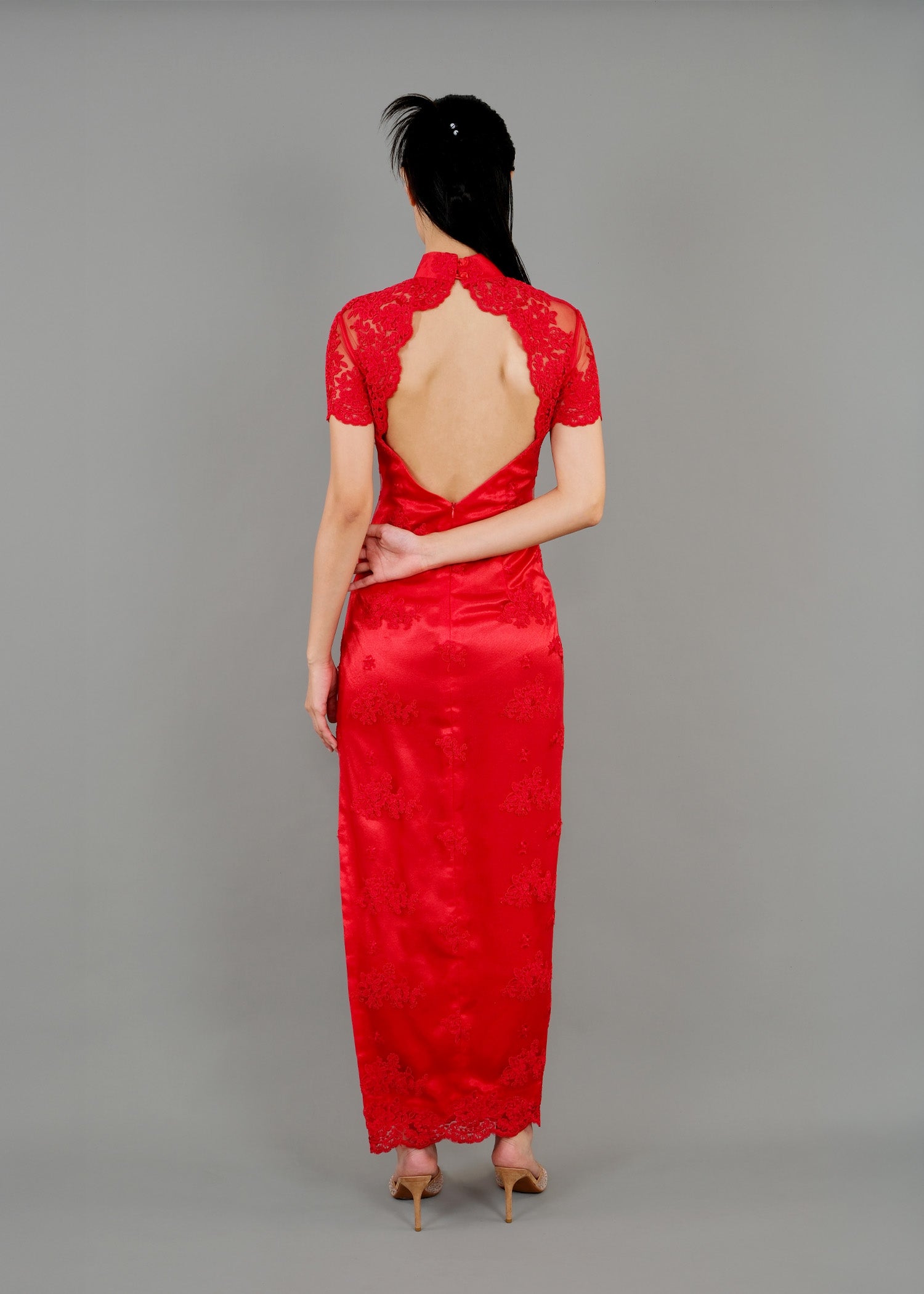 A woman stands in back view, wearing a red high-neck dress with sheer sleeves and floral lace details, featuring an open back.
一名女子背影中，身穿紅色高領連身裙，透明袖子上飾有花卉蕾絲，露背設計。