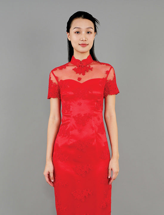An asian woman wearing a short sleeve lace sheath qipao with transparent mesh upper body against a gray background.
一位亞洲女子，身著短袖蕾絲修身旗袍，上身為透明網紗設計，以灰色背景襯托。