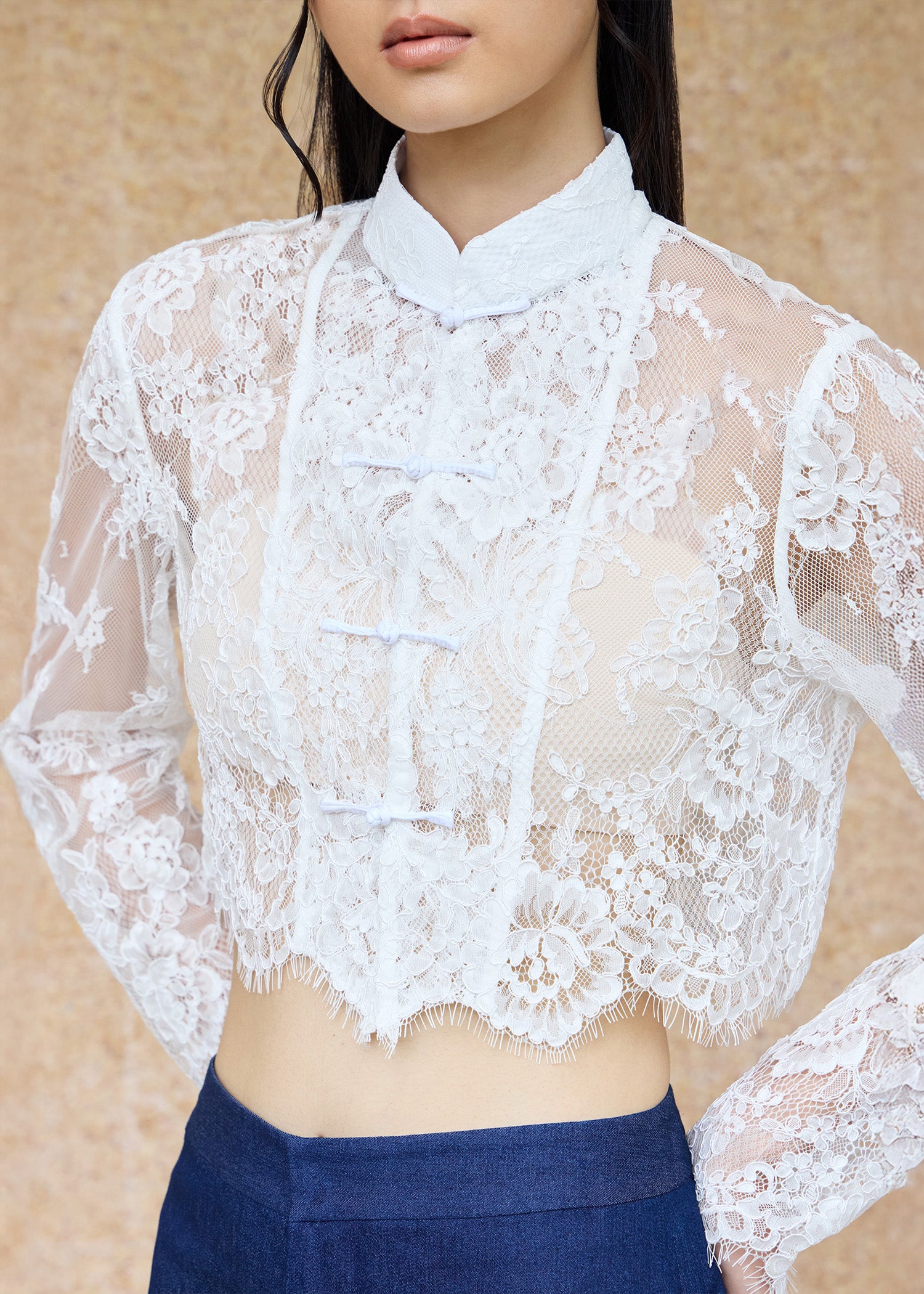 Front view, half-body shot of an Asian woman wearing a long sleeve lace qipao jacket by Qipology, set against a yellow-beige background.