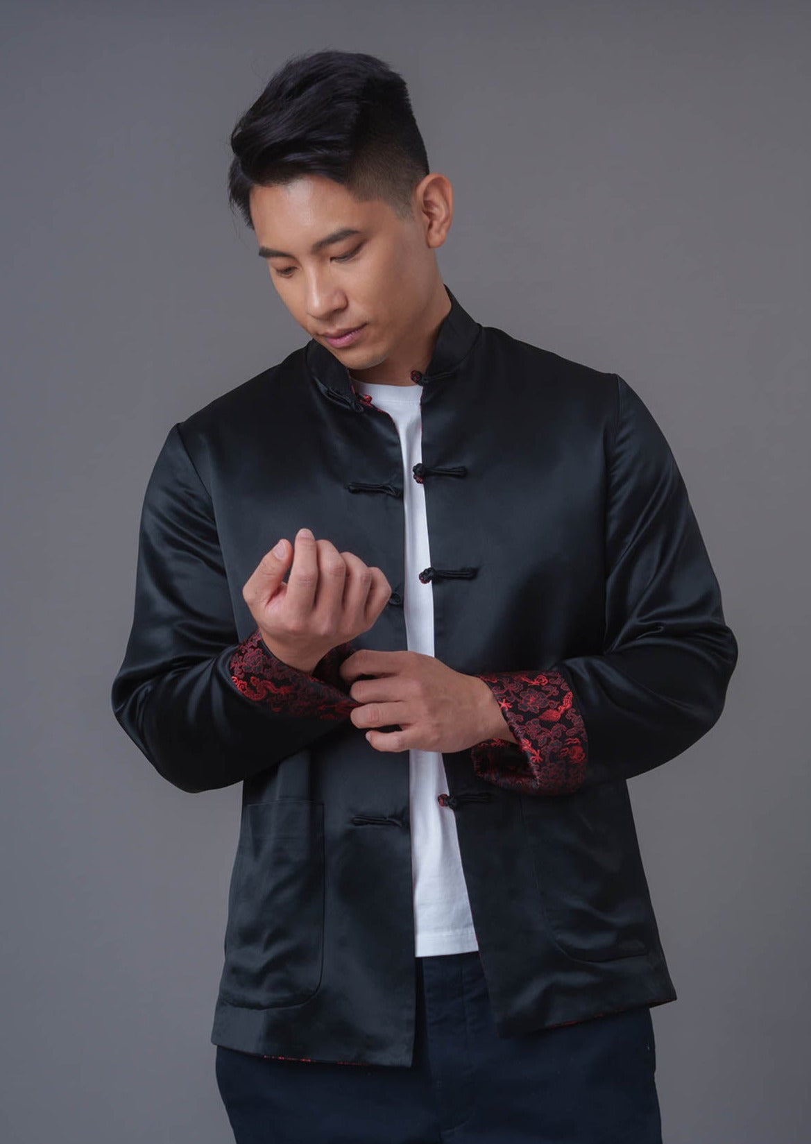 An asian Man wearing a black stain x red tiger brocade Tang Jacket against a gray background. 一位亞洲男子，以灰色為背景，穿著黑色緞面與紅色虎紋錦緞的唐裝外套。