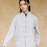 Front view, half-body shot of an Asian woman wearing a khaki grey knitted Tang jacket over a keyhole denim qipao top by Qipology, set against a yellow-beige background.