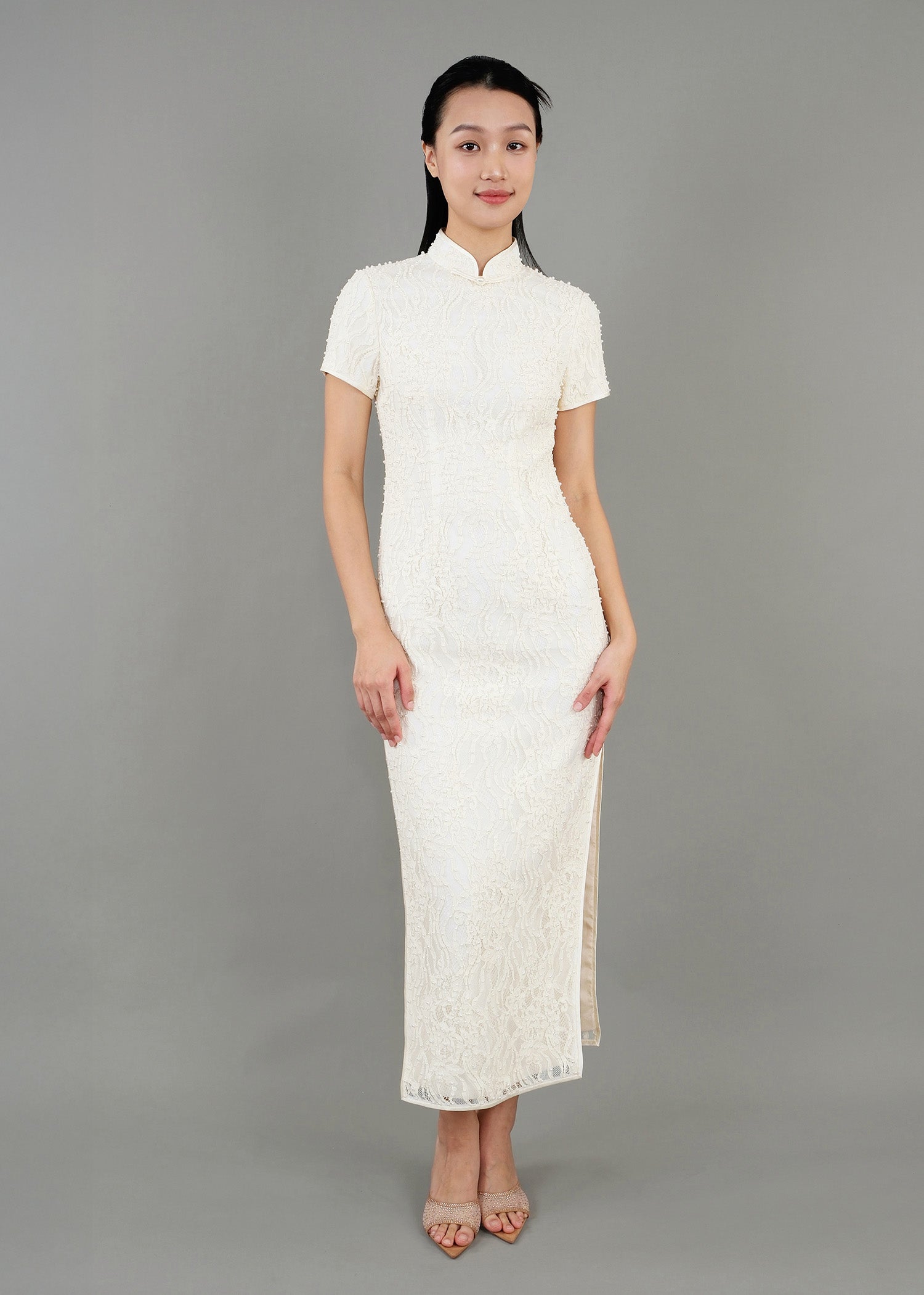 A woman stands in front view, wearing a white high-neck dress with short sleeves and textured detailing, featuring a side slit.
一名女子站在正面，穿著白色高領連身裙，短袖，帶有紋理細節和側開衩。