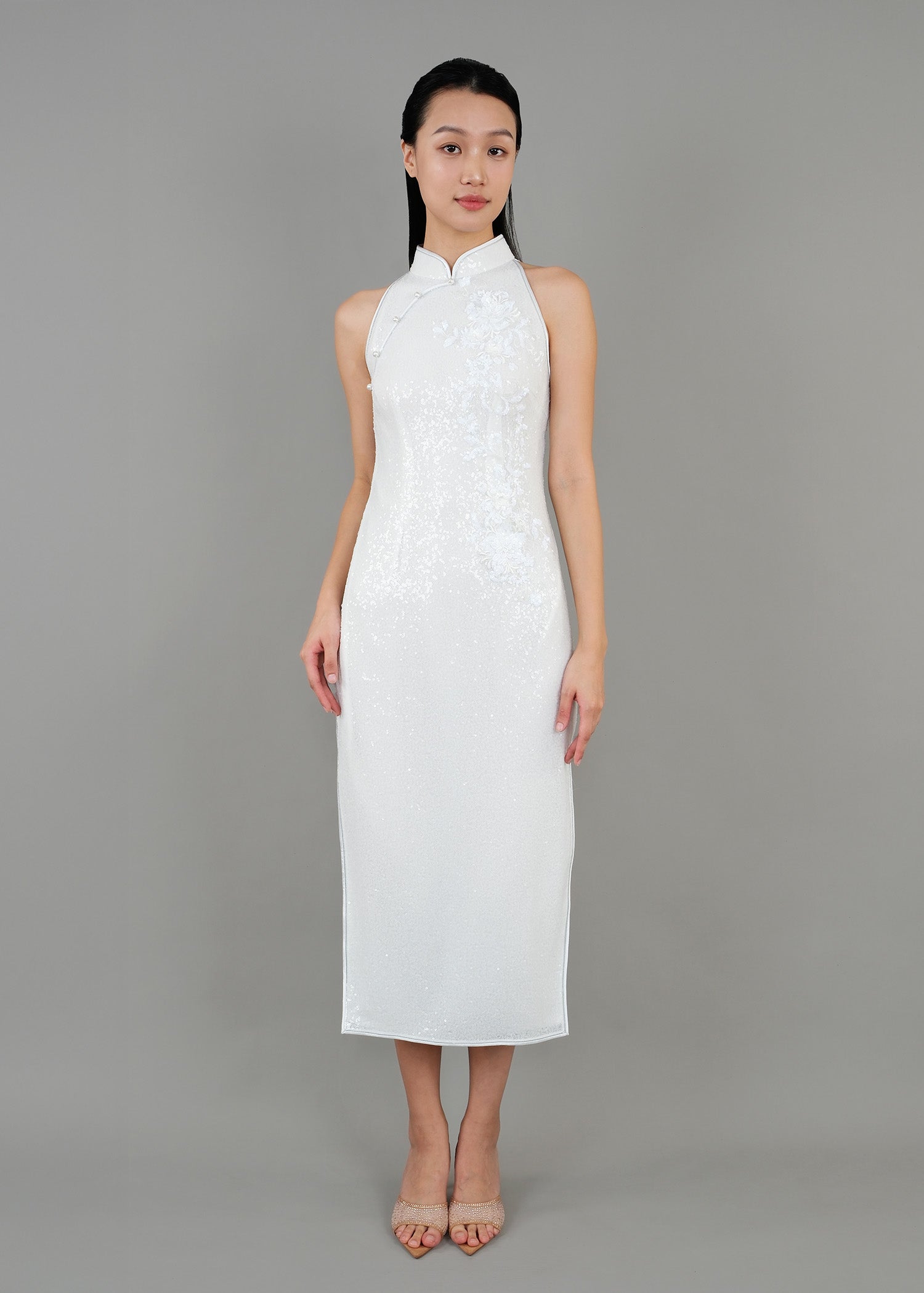 A woman is wearing a white high-neck dress that features delicate floral patterns. The dress has a fitted silhouette and falls to the knee.
一名女子身穿一件白色高領連身裙，裙上飾有精緻的花卉圖案。這件洋裝剪裁合身，長度達膝蓋。