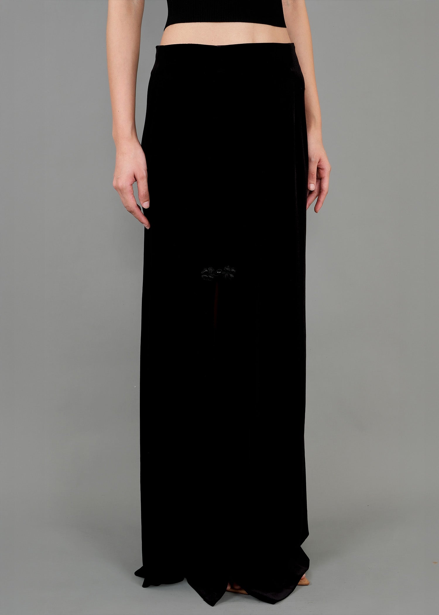 A close-up of a black dress featuring a slit on the left side, revealing a hint of leg. The dress is elegant and form-fitting, with a subtle floral detail near the slit. The fabric has a soft sheen, enhancing its luxurious appearance.
特寫鏡頭展現了一件黑色連身裙，左側開衩，隱約露出腿部肌膚。洋裝優雅修身，開衩附近點綴著精緻的花朵圖案。布料散發著柔和的光澤，更添奢華質感。