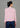 A woman stands in back view, wearing a pink high-neck short-sleeved top paired with loose blue pants, showcasing a fashionable casual style.
一名女子的背影，穿著粉紅色的高領短袖上衣，搭配寬鬆的藍色褲子，展現出時尚的休閒風格。