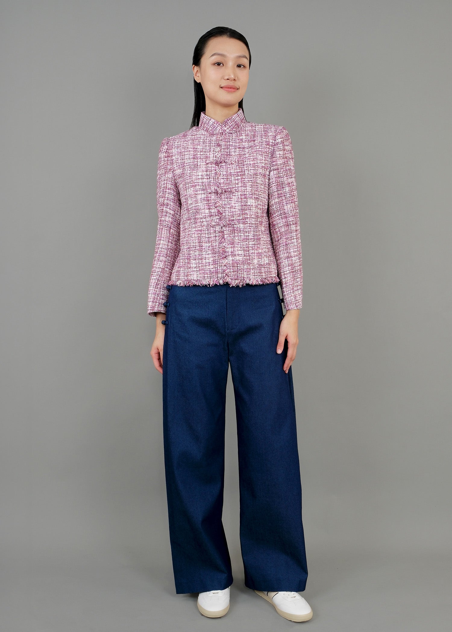 A woman stands in front view, wearing a pink textured jacket with a high collar and long sleeves, paired with wide-legged blue pants. She completes the outfit with white sneakers.
一名女子站在正面，身穿黑色亮片高領長袖外套和粉紅色紋理高領長袖外套，搭配藍色寬褲。她腳踩白色運動鞋，褲子開衩。
