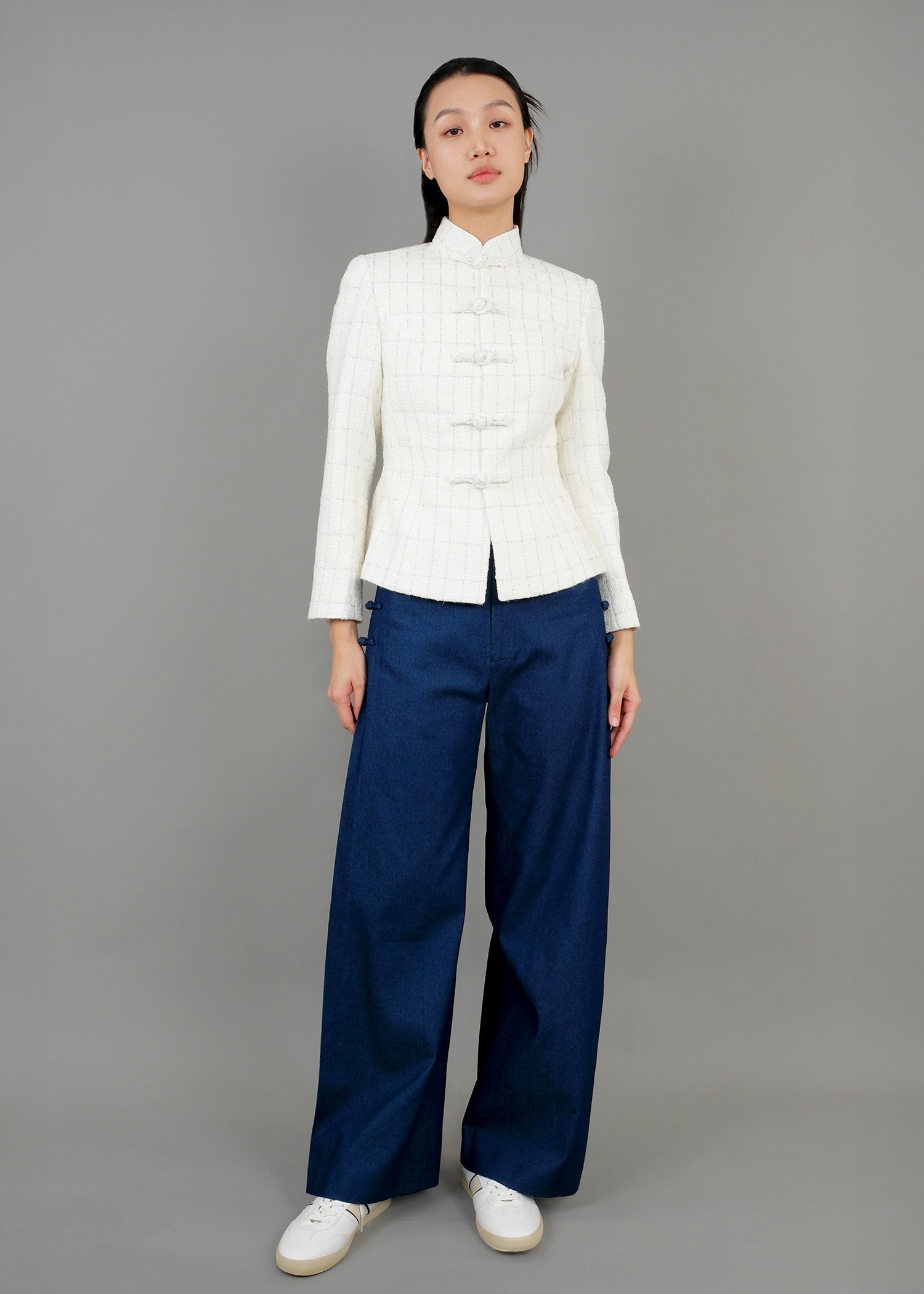 A woman stands in front, wearing a white high-collared jacket with button details and loose-fitting dark blue wide-leg trousers, paired with white sneakers, showcasing a modern and elegant style.
一名女子站在正面，身穿白色高領外套，具有連結細節，搭配寬鬆的深藍色寬褲和白色運動鞋，展現出摩登優雅的風格。