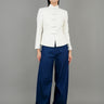 A woman stands in front, wearing a white high-collared jacket with button details and loose-fitting dark blue wide-leg trousers, paired with white sneakers, showcasing a modern and elegant style.
一名女子站在正面，身穿白色高領外套，具有連結細節，搭配寬鬆的深藍色寬褲和白色運動鞋，展現出摩登優雅的風格。