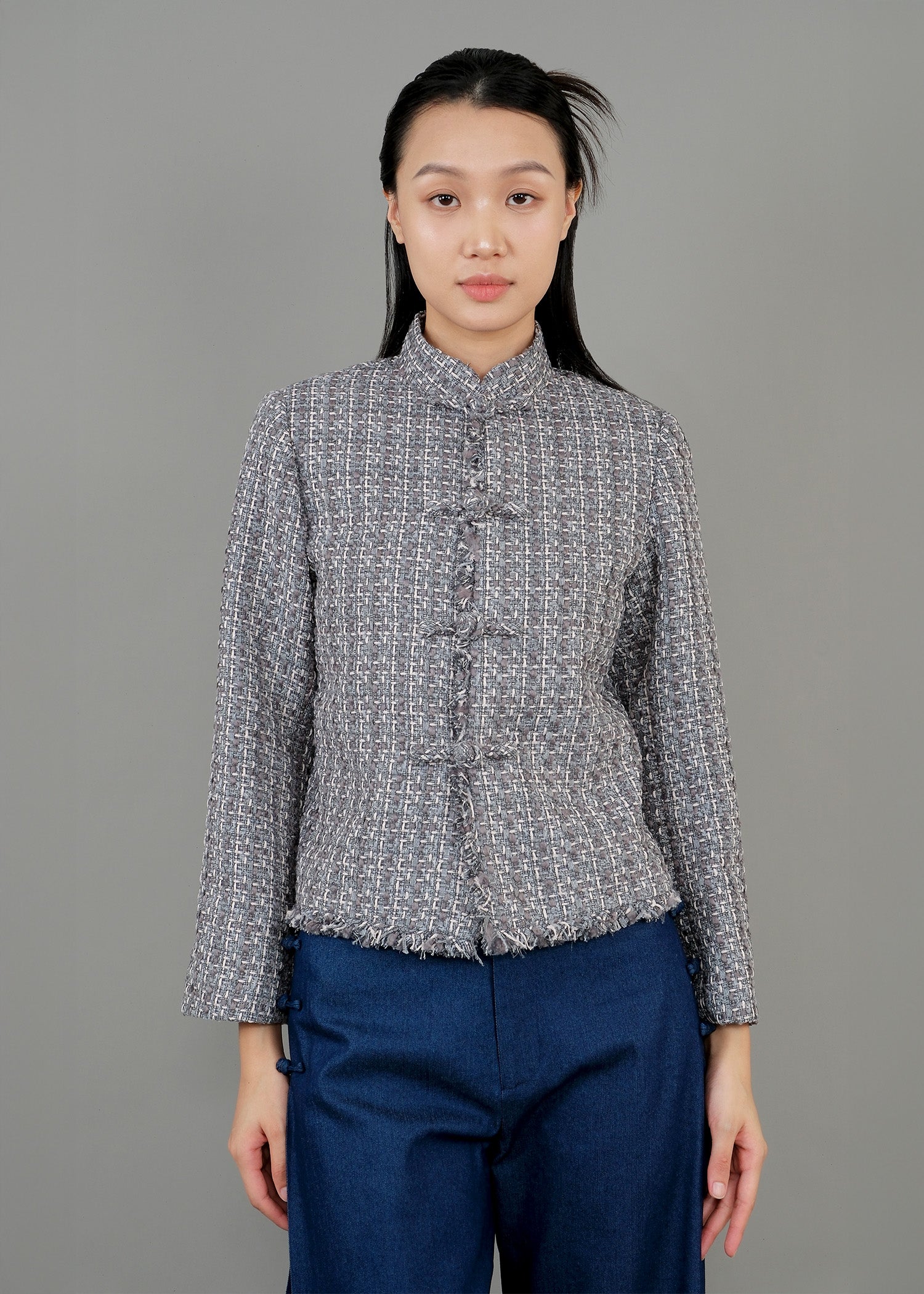 A woman stands in front, wearing a textured green gray button-up top with a high collar and loose blue pants, exuding a modern and sophisticated style.
一名女子站在正面，身穿綠灰色高領質感紐扣上衣，搭配寬鬆藍色褲子，展現出現代精緻的風格。
