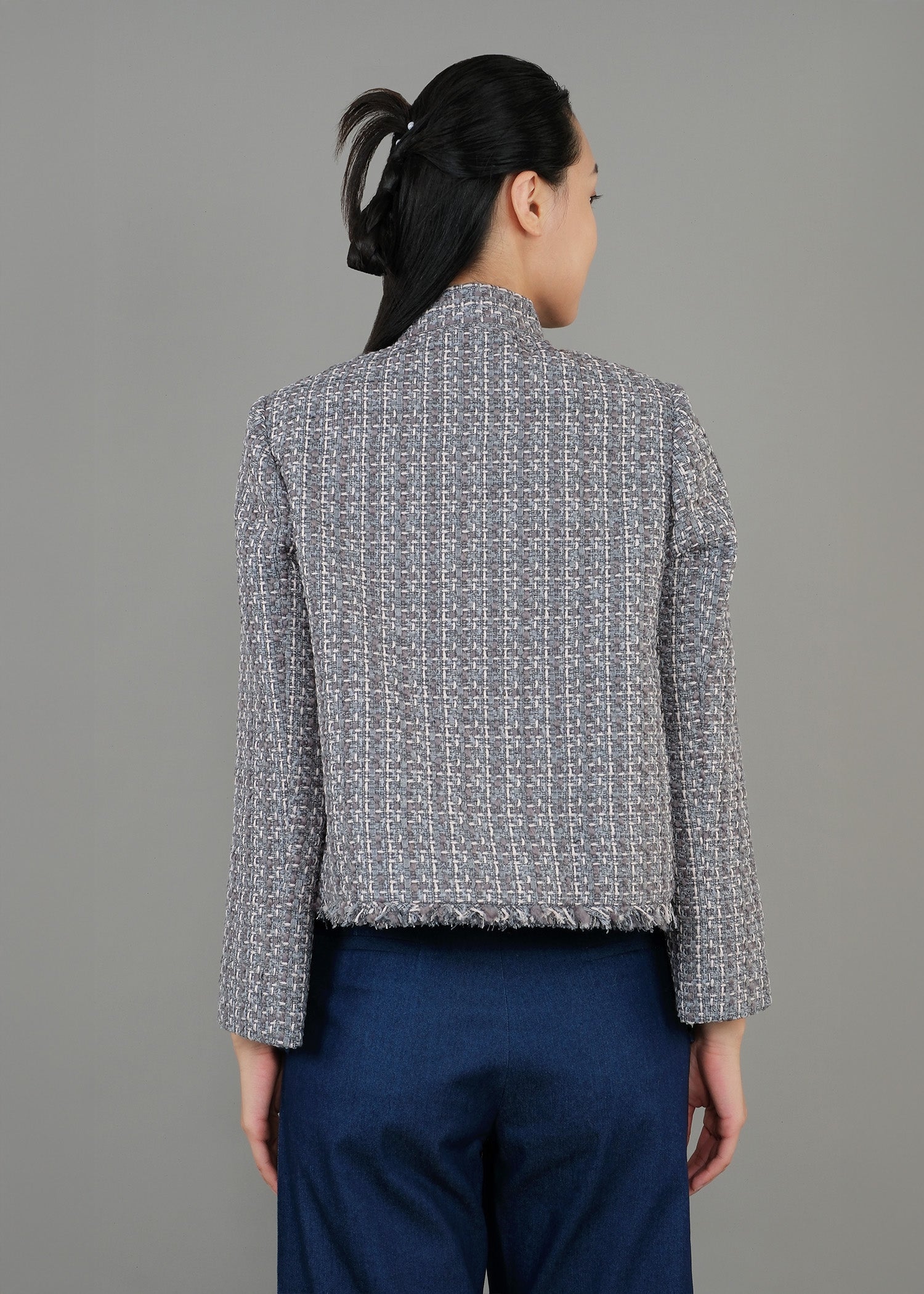 A woman stands in back view, wearing a textured green gray button-up top with a high collar and loose blue pants, exuding a modern and sophisticated style.
一名女子的背影，身穿綠灰色高領質感紐扣上衣，搭配寬鬆藍色褲子，展現出現代精緻的風格。
